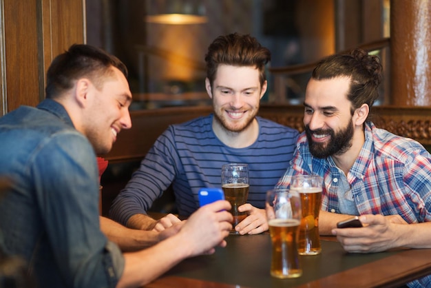 Concetto di persone, uomini, tempo libero, amicizia e tecnologia - amici maschi felici con smartphone che bevono birra al bar o al pub