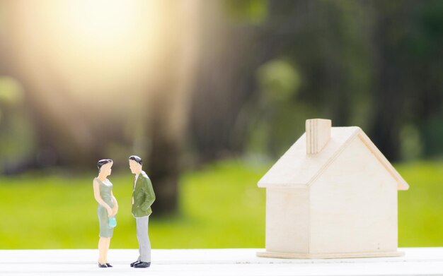 people model with small house on table with green park background