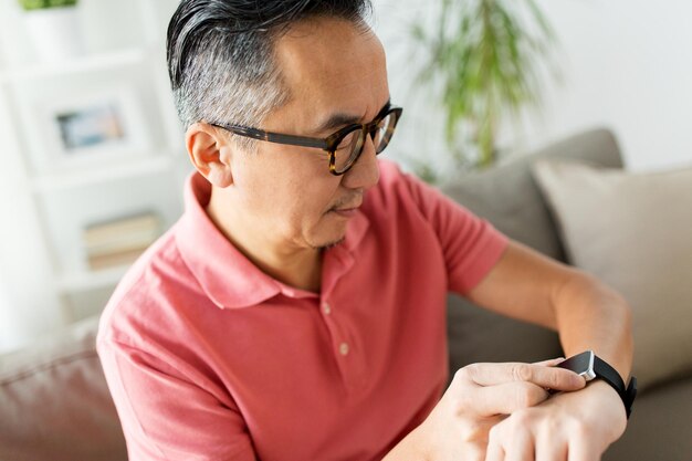 Foto persone, tecnologia moderna e concetto di tempo - primo piano di un uomo asiatico con un orologio intelligente a casa