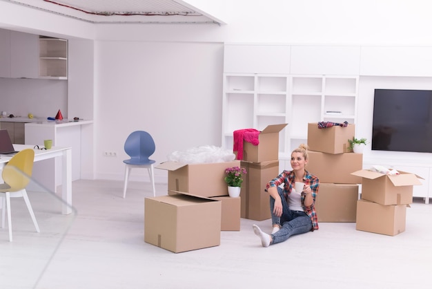 people, moving new place and repair concept   happy beautiful  young woman with many cardboard boxes sitting on floor with Cup at home