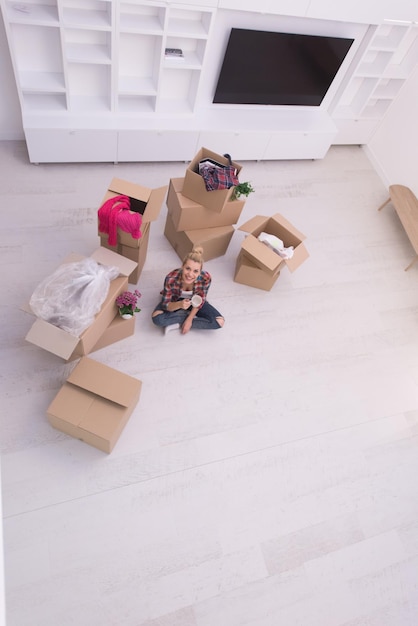 people, moving new place and repair concept   happy beautiful  young woman with many cardboard boxes sitting on floor with Cup at home