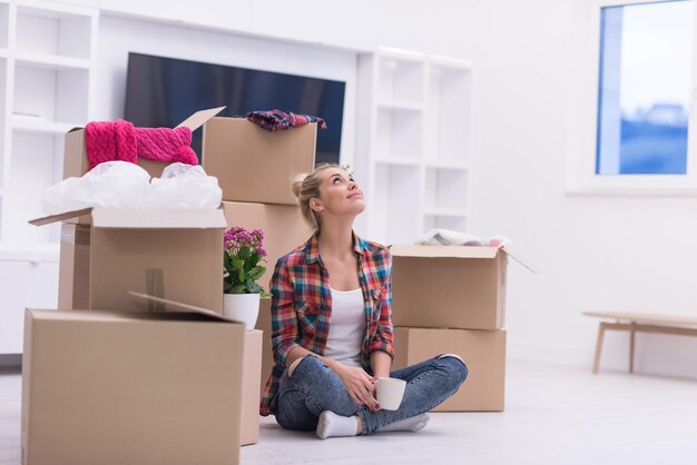 people, moving new place and repair concept   happy beautiful  young woman with many cardboard boxes sitting on floor with Cup at home