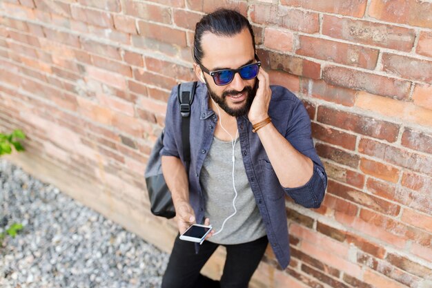 people, music, technology, leisure and lifestyle - hipster man with earphones on city street listening to music