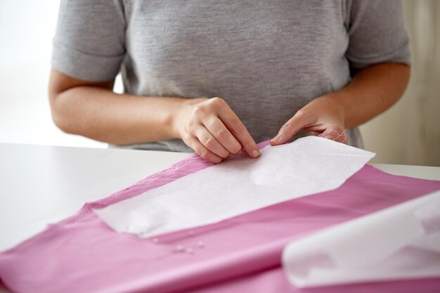 Foto concetto di persone, cucito e sartoria: donna su misura con spille che cuce modello di carta su tessuto nello studio di cucito