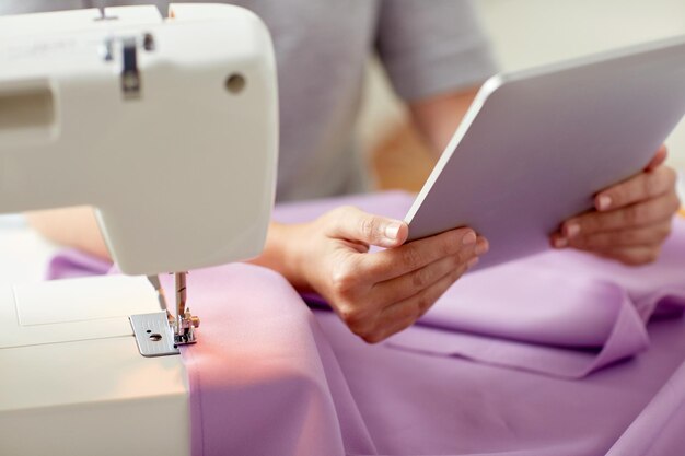 Photo people, needlework, technology and tailoring concept - tailor woman with sewing machine, tablet pc and fabric