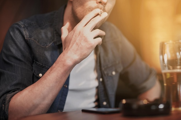 people, nicotine addiction and bad habits concept - close up of man drinking beer and smoking cigarette at bar or pub