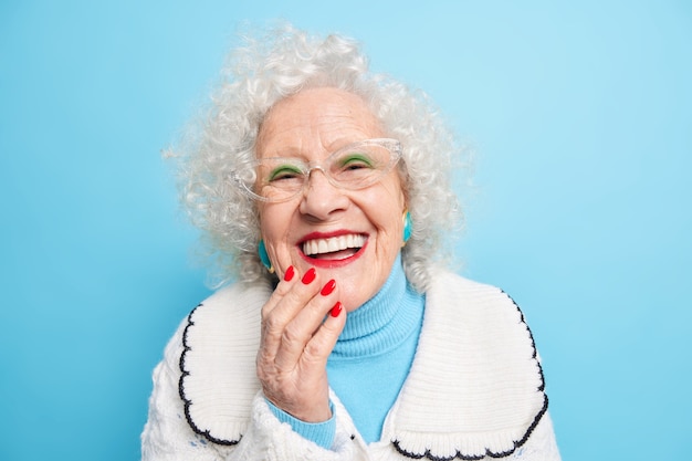 Concetto di emozioni positive di vecchiaia della gente. felice signora dai capelli grigi sorride ampiamente ha denti bianchi e uniformi indossa un trucco luminoso