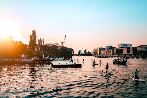 Люди катаются на веслах по реке по городу на чистом небе во время захода солнца