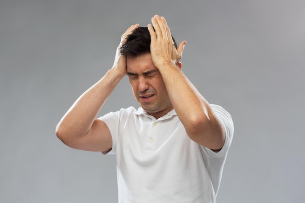 people, pain and stress concept - unhappy man suffering from head ache over gray background