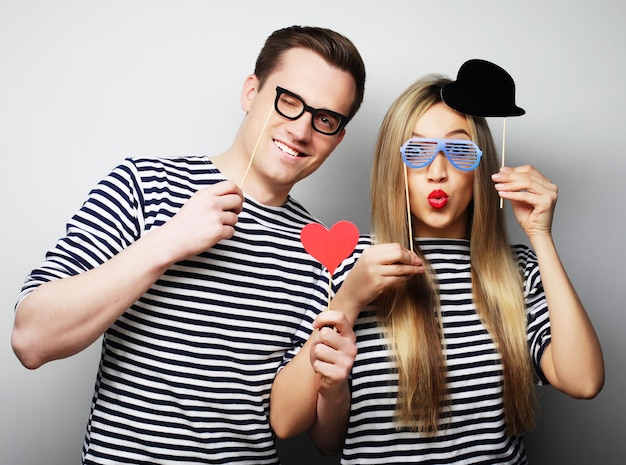 파티 사랑과 여가 개념: 파티 안경과 모자를 들고 회색 배경의 막대기 위에 있는 사랑스러운 커플