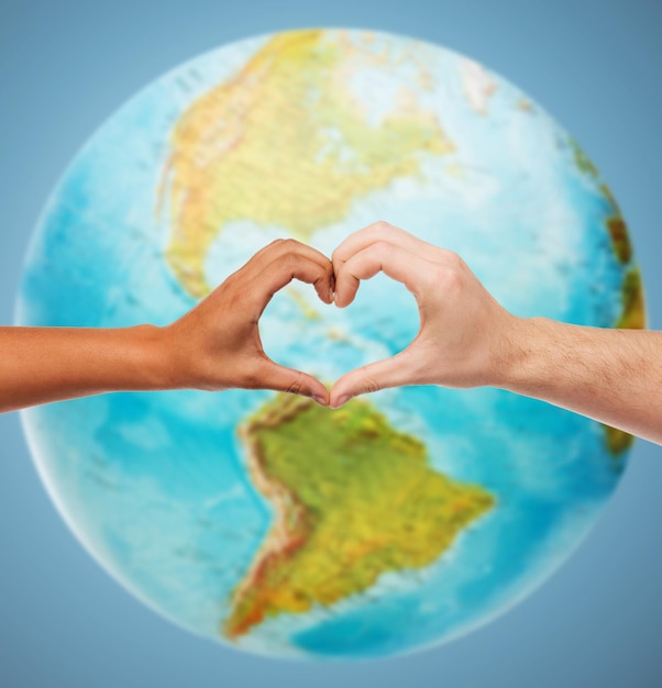 Фото Люди, мир, любовь, жизнь и экологическая концепция - крупный план человеческих рук, показывающий жест в форме сердца над земным шаром и синим фоном
