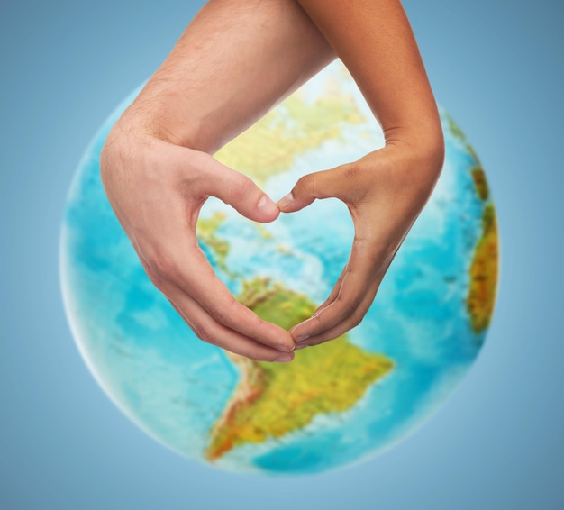 people, peace, love, life and environmental concept - close up of human hands showing heart shape gesture over earth globe and blue background