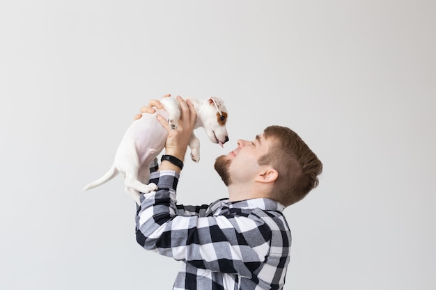 People, pets and animals concept - young man holding jack russell terrier puppy on white wall with copy space.