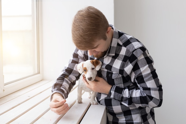 Concetto di persone, animali domestici e animali - giovane che abbraccia il cucciolo di jack russell terrier vicino alla finestra su sfondo bianco.