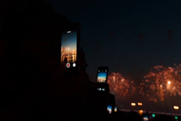 電話で花火のお祝いを撮影する人々。焦点はスマートフォンにあります。