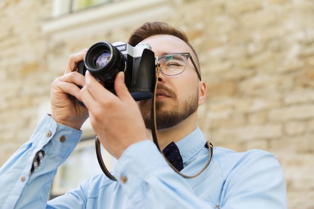 人、写真、技術、レジャー、ライフ スタイル - 街の通りでレトロなビンテージ フィルム カメラで写真を撮る幸せな流行に敏感な若い男