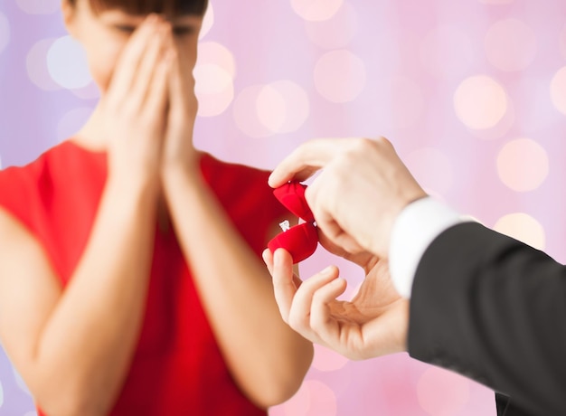 people, proposal, holidays, anniversary and presents concept - close up of couple with diamond engagement ring over holidays lights background