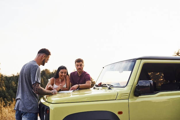 People reading map that lying on the hood of the automobile