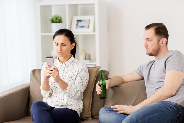 Photo people, relationship difficulties and conflict concept - man drinking beer and woman with smartphone having argument at home