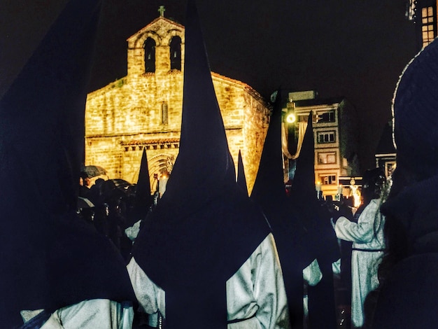 Foto persone in abiti religiosi in piedi vicino alla chiesa contro un cielo limpido di notte durante la settimana santa.