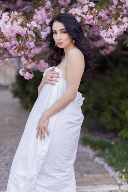 Concetto di persone, riposo, comfort e svago - giovane donna per le strade serali avvolta in una coperta. bella ragazza nel parco e un albero in fiore sakura