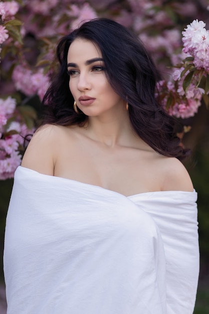 People, rest, comfort and leisure concept - Young woman through the evening streets wrapped in a blanket. Beautiful young girl in the park and a flowering tree sakura