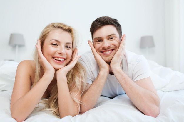 people, rest, love, relationships and happiness concept - happy couple lying in bed at home