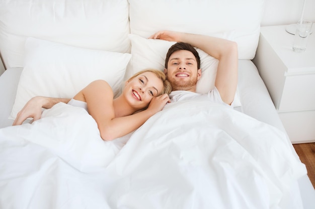 people, rest, love, relationships and happiness concept - happy smiling couple lying in bed at home