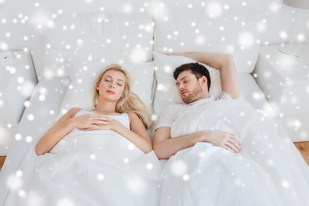 people, rest and relationships concept - happy couple sleeping in bed at home over snow