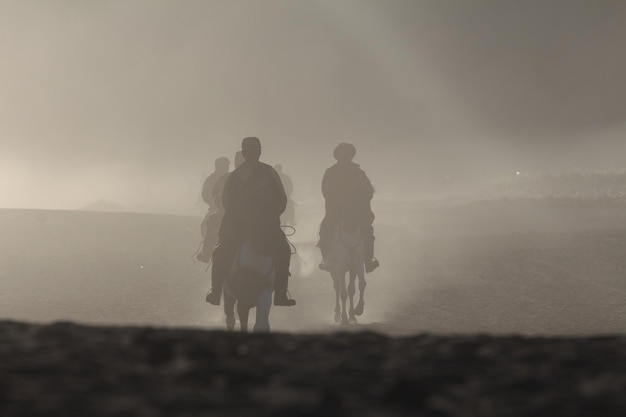 Foto persone a cavallo nel deserto durante il tempo nebbioso