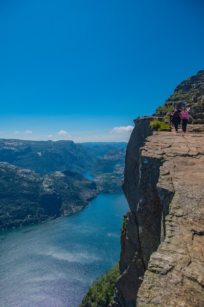 People on rock by mountains against blue sky