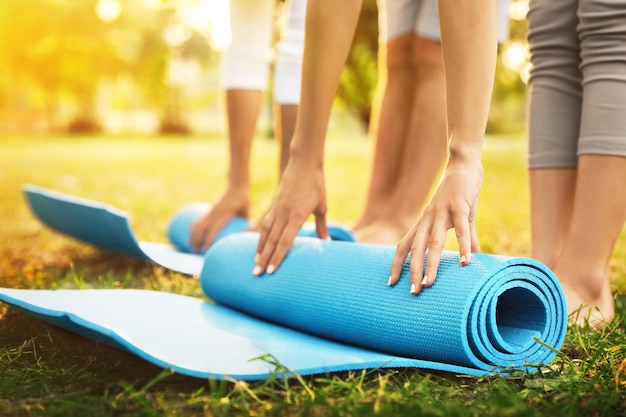 People rolling up yoga mats in park on sunny day closeup