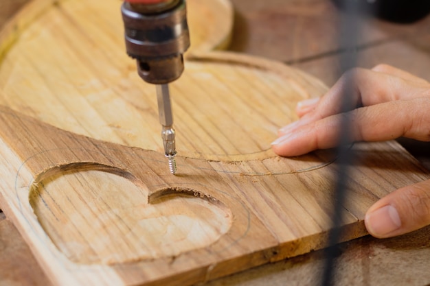 Foto le mani della gente usando la macchina del router che lavora al pavimento di legno della plancia di forma del cuore