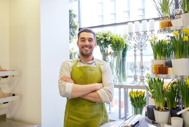 Foto concetto di persone, vendita, vendita al dettaglio, affari e floristica - uomo o venditore di fiorista sorridente felice in piedi al bancone del negozio di fiori