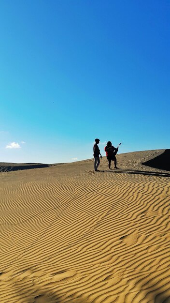 People on sand dune in desert against clear blue sky