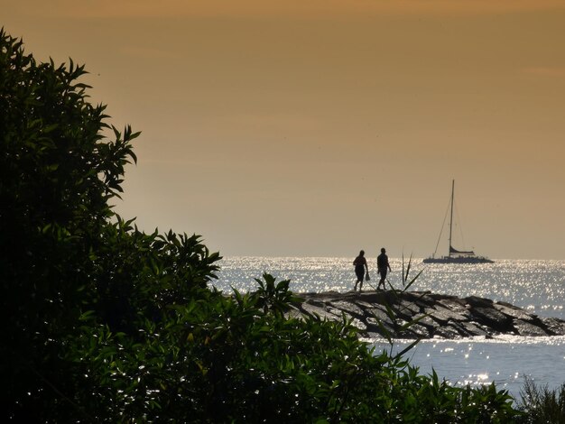 Photo people at seaside against sky during sunset