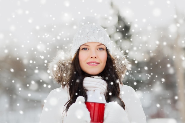 People, season, drinks and leisure concept - happy young woman with tea cup outdoors in winter