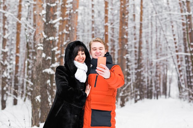 People, season, love, technology and leisure concept - happy couple taking picture with smartphone selfie stick on over winter background