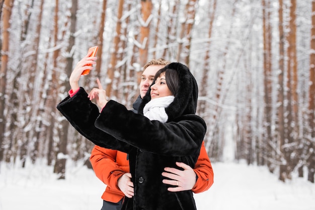 People, season, love, technology and leisure concept - happy couple taking picture with smartphone selfie stick on over winter background