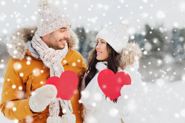 люди, сезон, любовь и концепция дня святого валентина - счастливая пара, держащая пустые красные сердца над зимним пейзажем