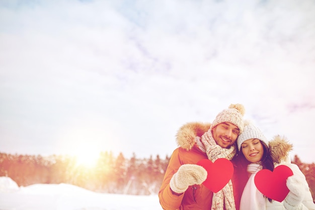 people, season, love and valentines day concept - happy couple holding blank red hearts over winter landscape