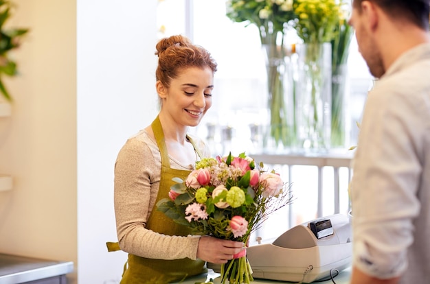 people, shopping, sale, floristry and consumerism concept - happy smiling florist woman making bouquet for and man or customer at flower shop