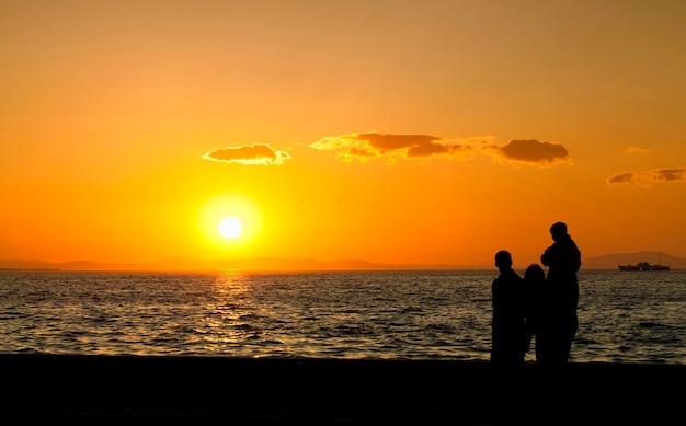 人々のシルエットと午後の光に沈む夕日の海