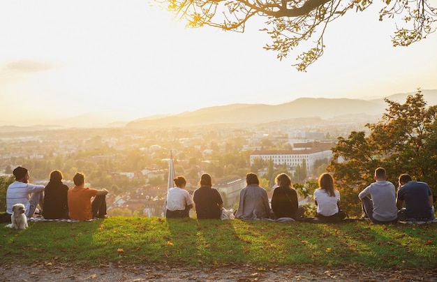 Люди сидят на горе и любуются закатом над осенней Любляной