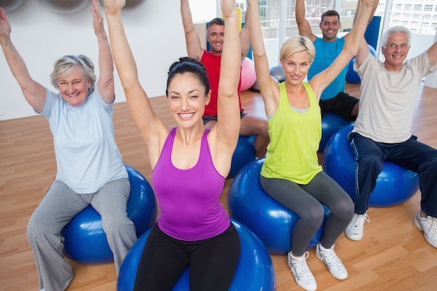 People sitting on exercise balls with hands raised