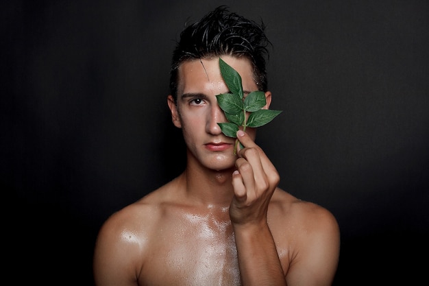 People, skincare and beauty concept - Wet young man with black hair on a black background. Portrait male with shaved chest . Men's skin care. Ripped muscular handsome man on black background