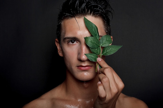 People, skincare and beauty concept - Wet young man with black hair on a black background. Portrait male with shaved chest . Men's skin care. Ripped muscular handsome man on black background