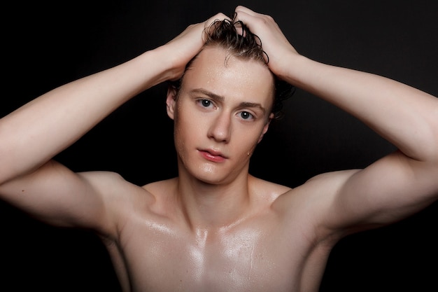 People, skincare and beauty concept - Wet young man with black hair on a black background. Portrait male with shaved chest . Men's skin care. Ripped muscular handsome man on black background