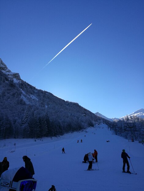 People on snow covered landscape against blue sky