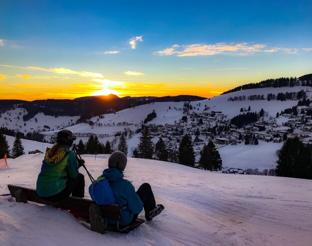 People on snow covered mountain against sky during sunset